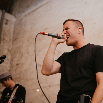 Unser Sänger Moritz singt kraftvoll in sein Mikrofon. Im Lingen Bildrand kann man unseren Bassisten Torsten erkennen.